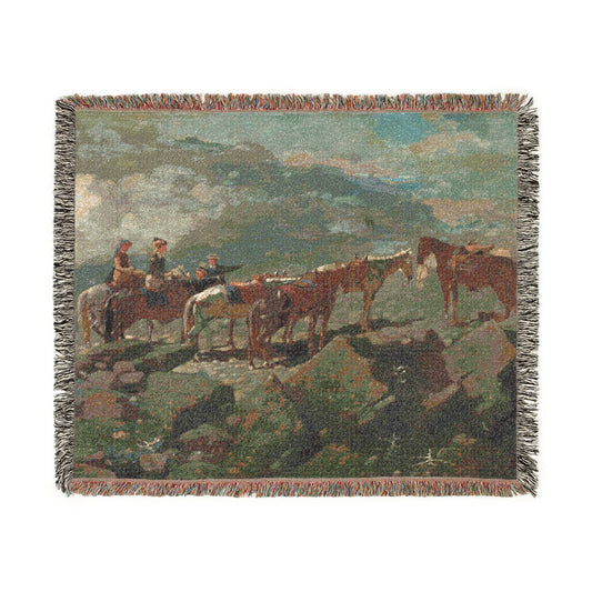 A woven throw blanket featuring a western landscape scene with horses and riders, finished with fringed edges.
