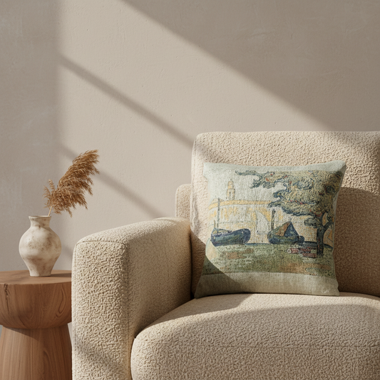 A square decorative throw pillow with a vintage-style scenic print of boats and trees, styled on a textured beige boucle armchair next to a wooden side table with a vase.