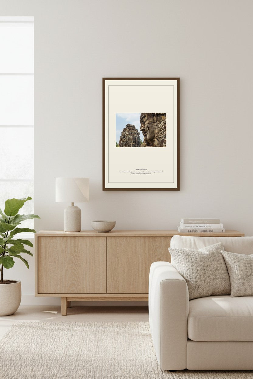 framed Bayon temple faces photograph above a light wood sideboard beside a table lamp and books
