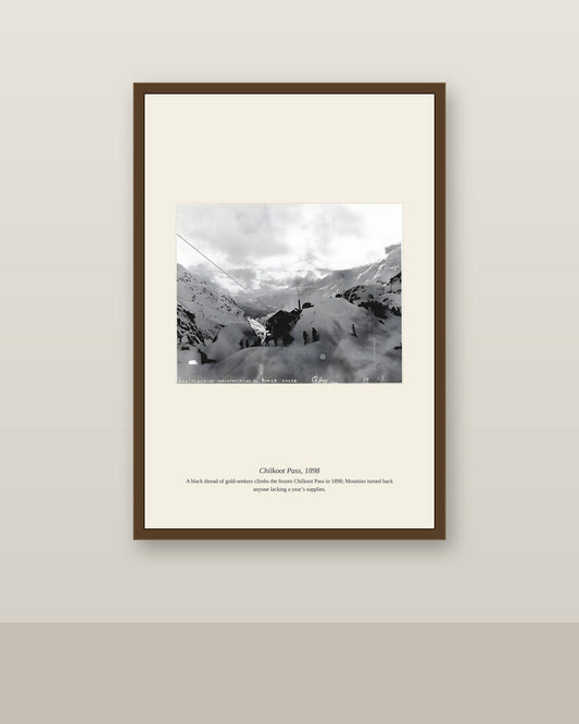 Chilkoot Pass photo in a slim brown frame on a neutral wall above a light baseboard