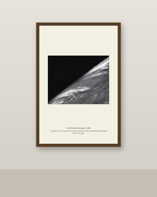 First Photo from Space print in a walnut frame on a neutral gray wall above empty floor space
