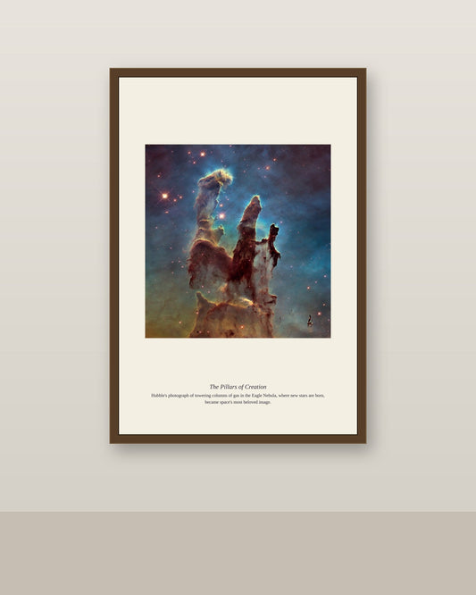 framed Pillars of Creation nebula print hanging in a coastal-style living room with white curtains and a blue-accented sofa