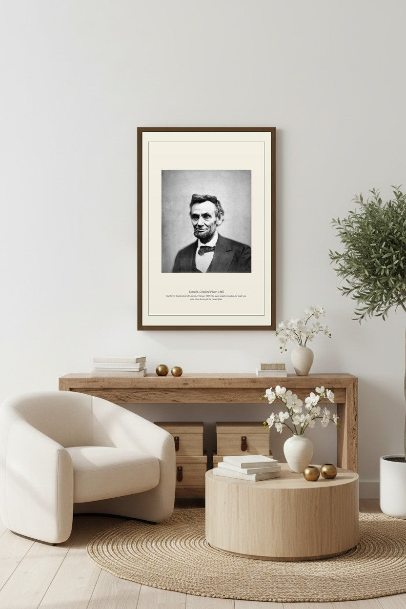 Framed Lincoln Cracked Plate print above a light wood console with a white armchair nearby
