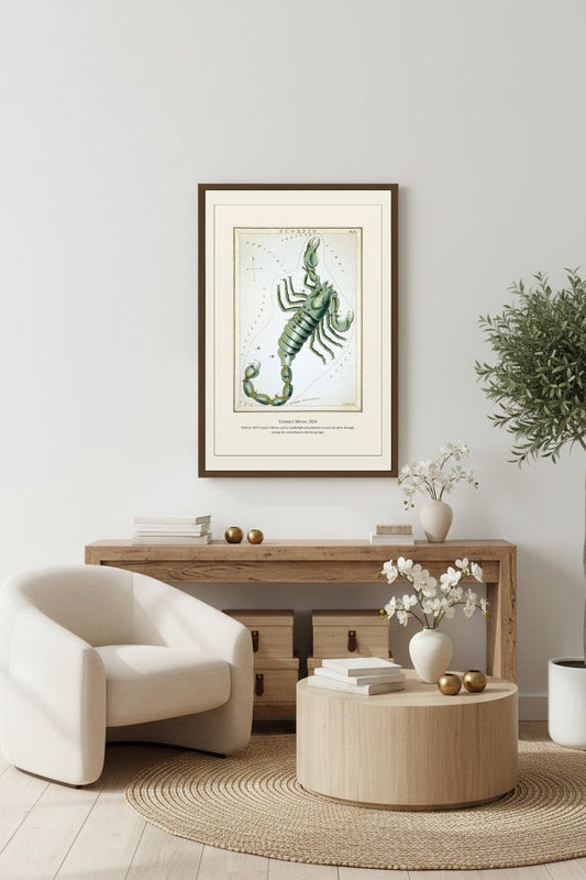 Framed Urania's Mirror print above a light wood console beside a cream armchair