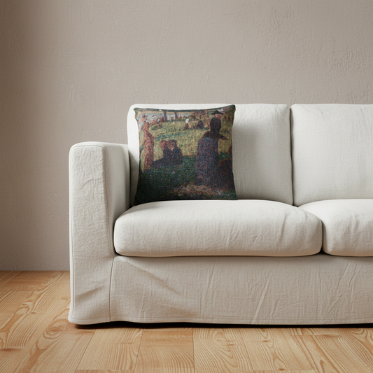 A square throw pillow featuring an impressionist-style painting of figures in a field, styled on a cream-colored fabric sofa over a light wood floor against a neutral beige wall.