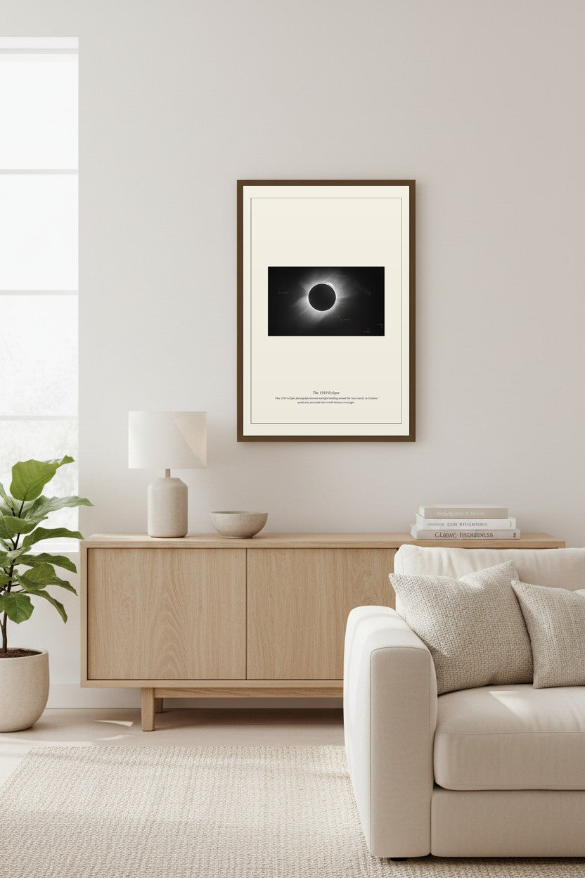 1919 Eclipse print above a light wood sideboard beside a potted fiddle-leaf plant