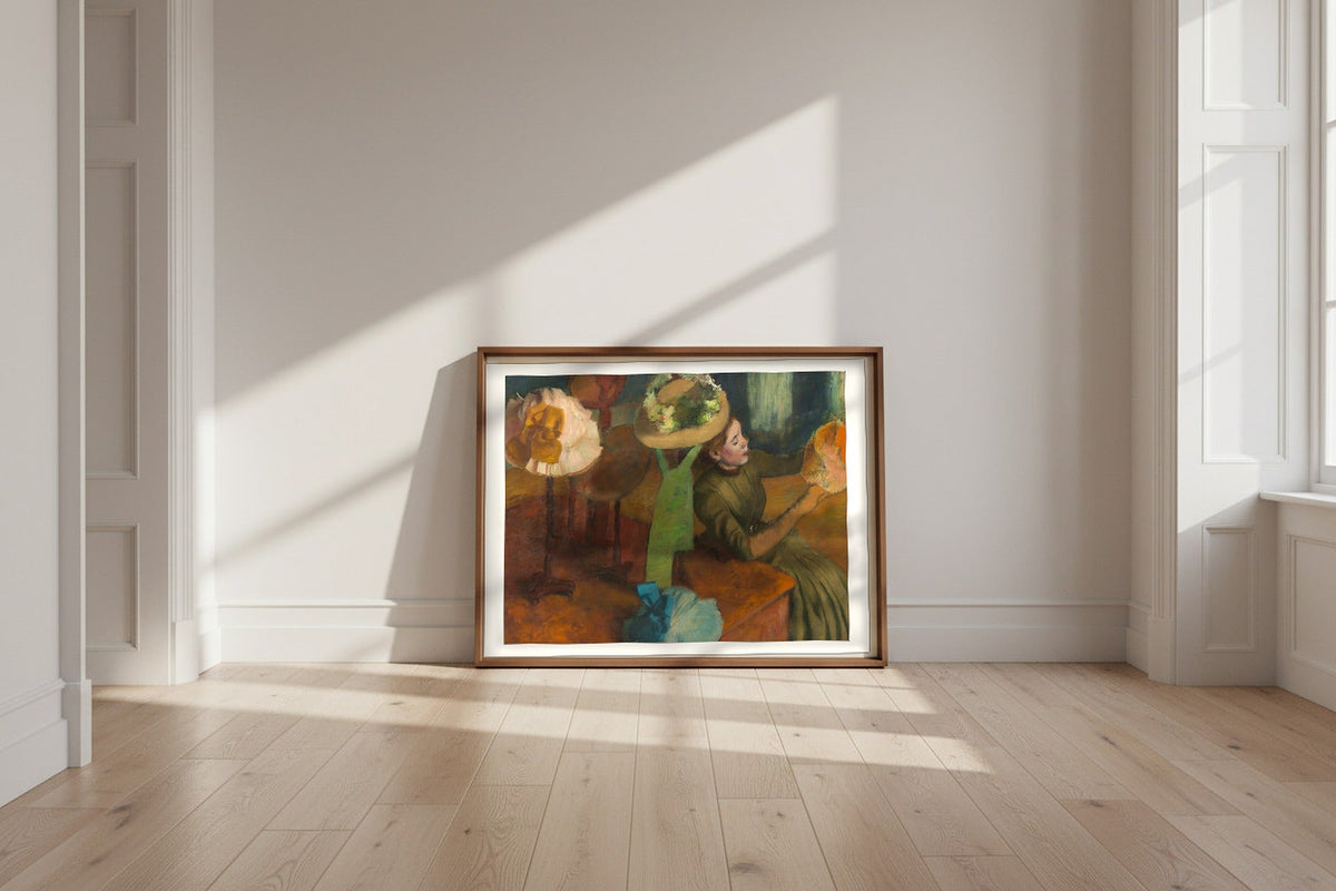 The Millinery Shop — Edgar Degas Fine Art Poster shown framed and leaning against a wall in a sunlit room