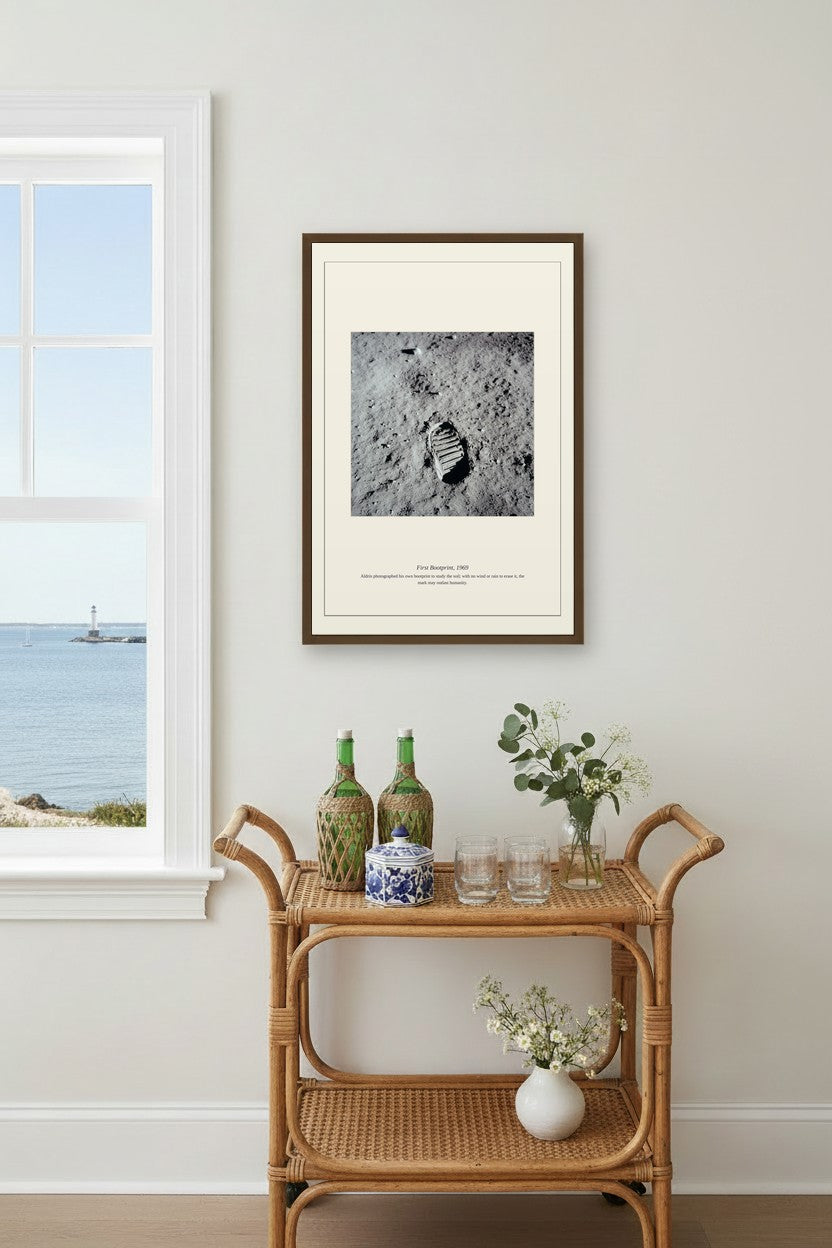 Framed First Bootprint photo above a rattan bar cart near a window with an ocean view