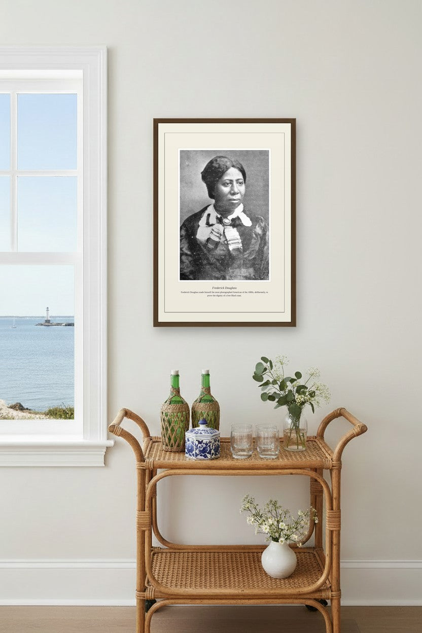 Frederick Douglass print in a dark frame above a rattan bar cart near an ocean-view window
