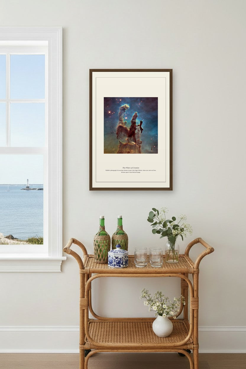 framed Pillars of Creation nebula print above a rattan bar cart beside a window with a coastal view