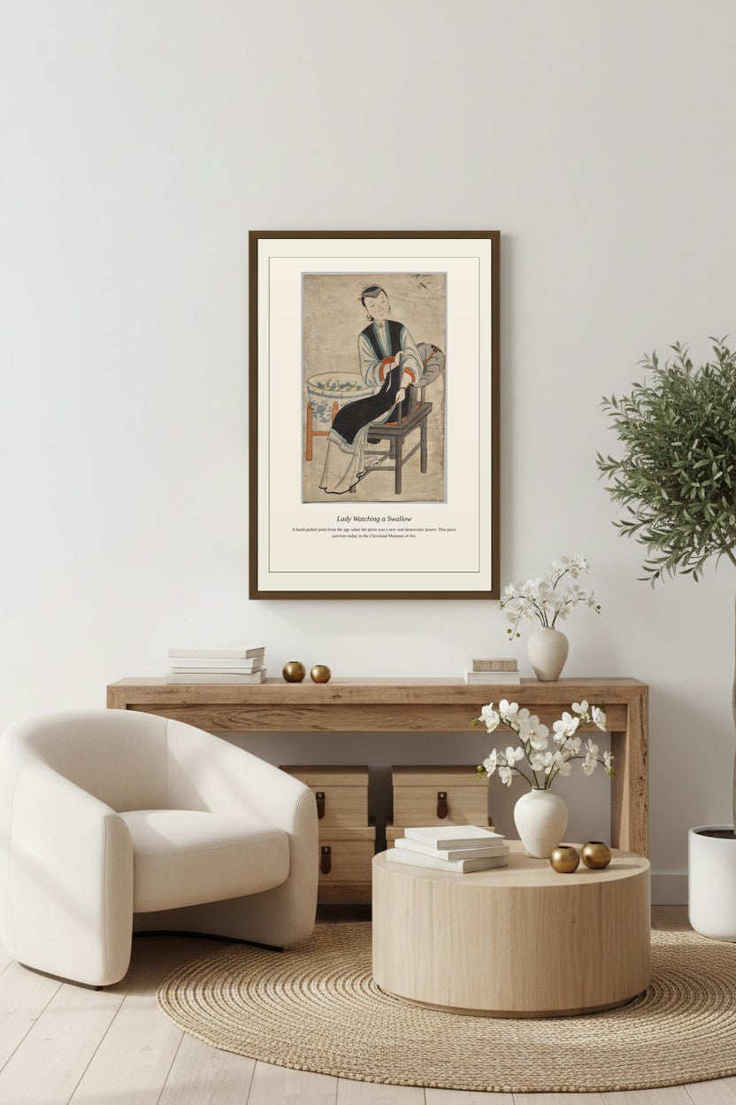 framed painting of a seated woman above a wooden sideboard beside a cream armchair on a round rug