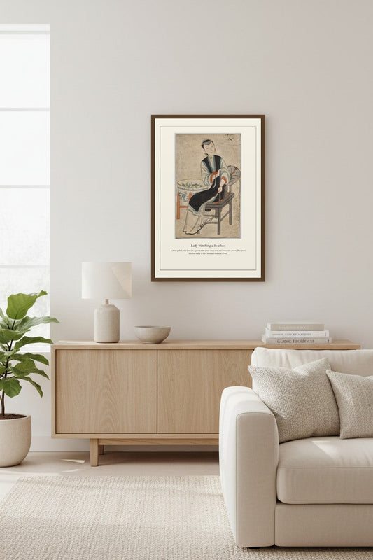 framed painting of a seated woman above a light wood sideboard beside a cream armchair