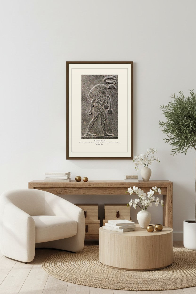 Framed Narmer Palette print above a wood console table with a bouclé chair and olive tree