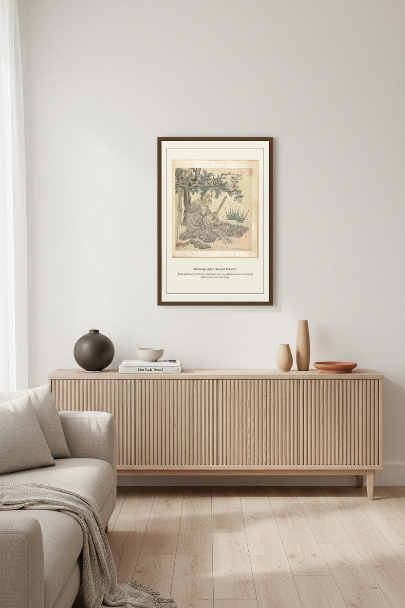 A framed art print featuring a vintage botanical illustration of a tree, styled on a light beige wall above a modern wooden sideboard in a minimalist living room setting.