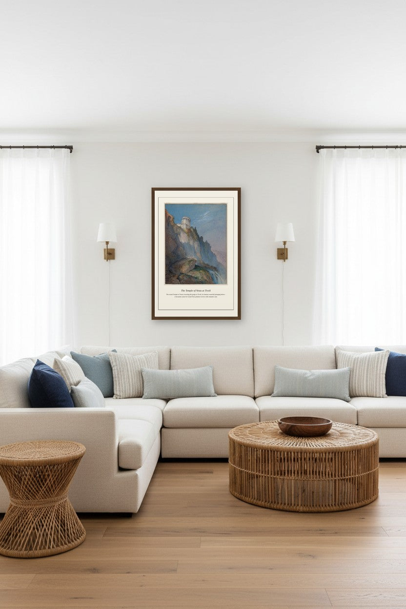 A framed landscape art print hangs on a white wall above a modern beige sectional sofa in a bright, contemporary living room with light wood floors, a round woven coffee table, and a matching side table.